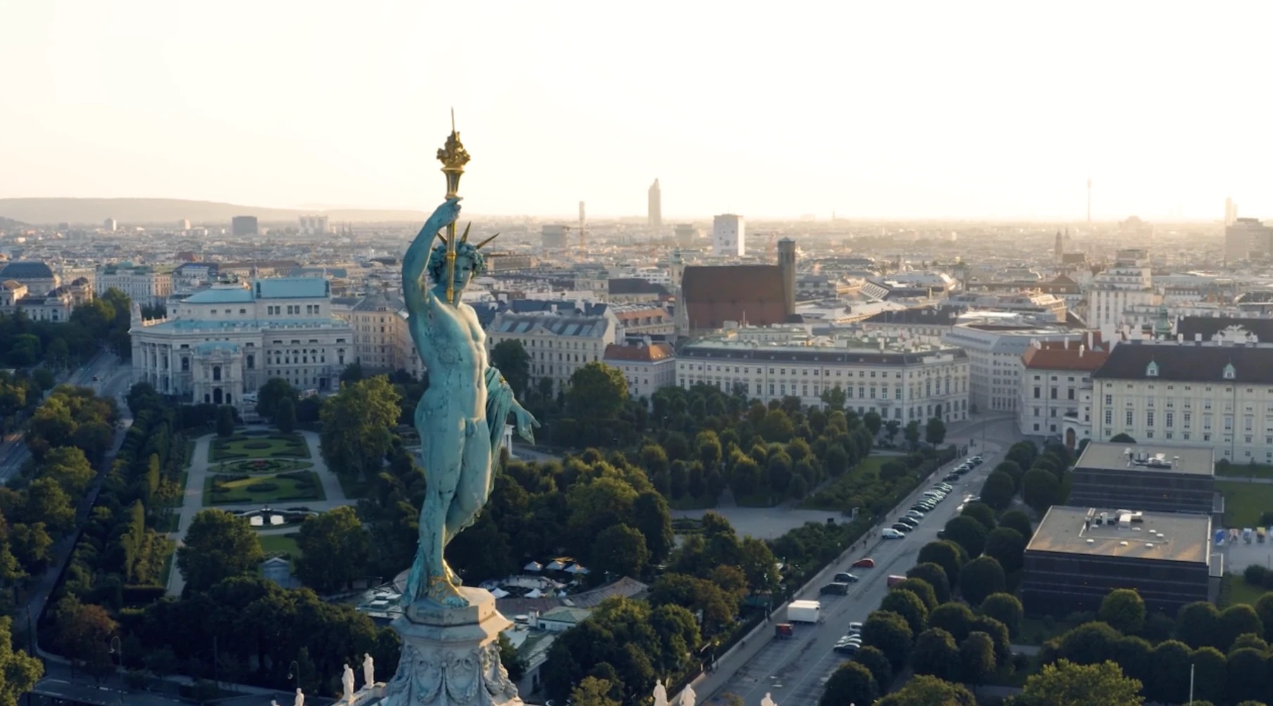 Luftaufnahme über Wien: Helios-Statue auf der Kuppel des Naturhistorischen Museums, dahinter Volksgarten, Burgtheater und die Innenstadt im Morgenlicht